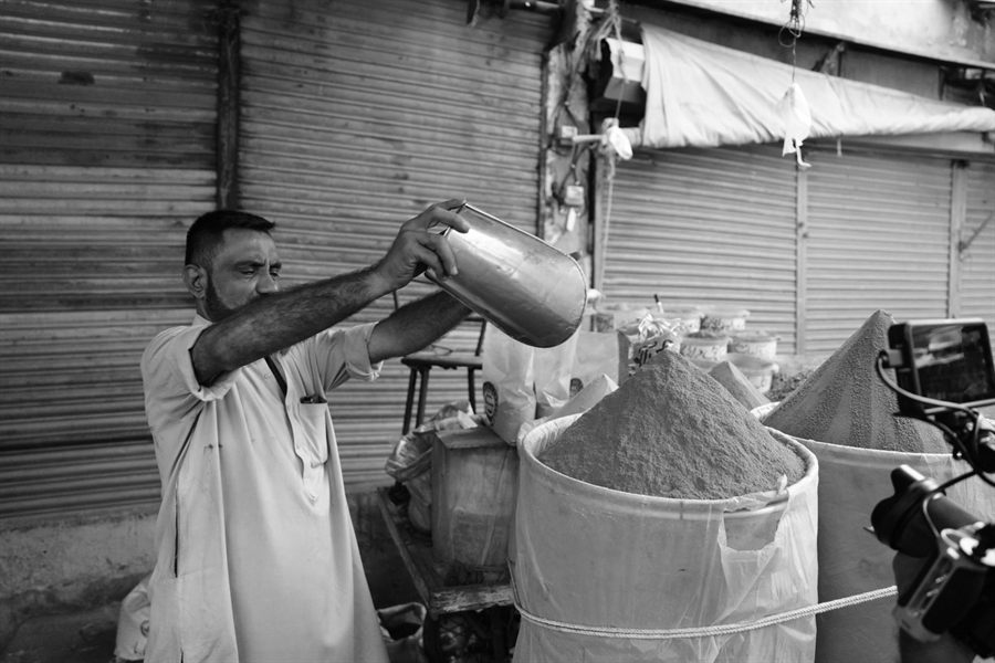 Black and white photo of a vendor pouring spices into a sack at an outdoor market
